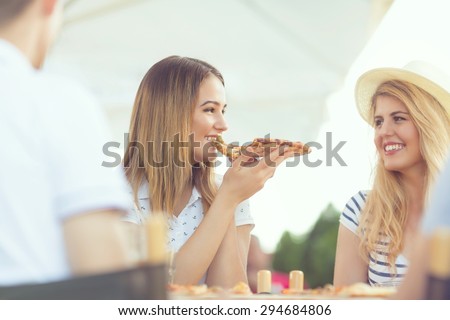 Pretty young girl eating slice of pizza with her friends in the restaurant