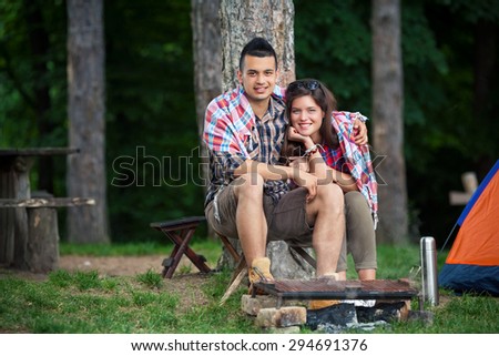 Young couple wrapped in blanket warming up by the fire in front of the tent