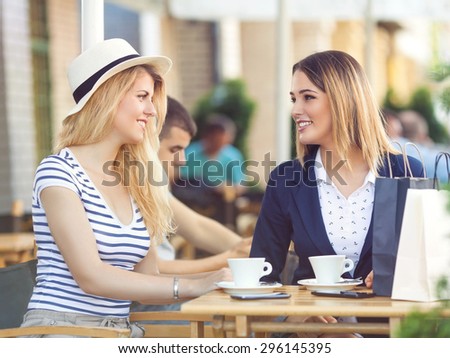 Two young girlfriends sitting in a cafe chatting and relaxing after successful shopping