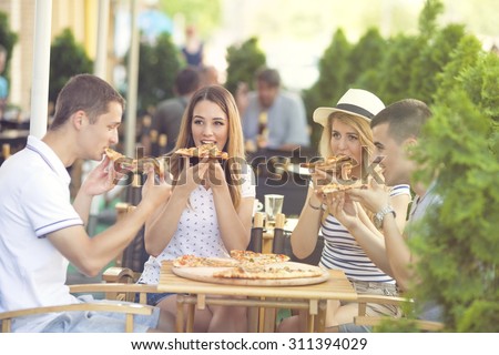 Group of four young people eating pizza in a restaurant