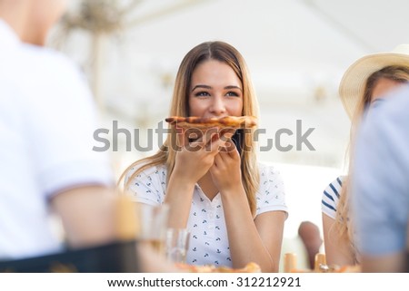 Pretty young girl eating slice of pizza with her friends in the restaurant