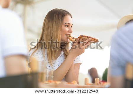 Portrait of pretty young girl sharing pizza with her friends in the restaurant
