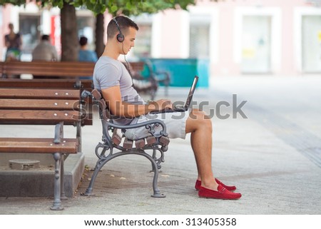 Busy young businessman working on his laptop while sitting on the park bench