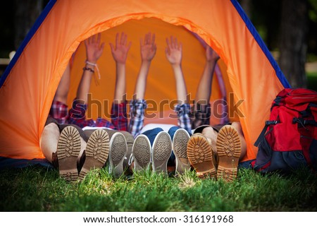 Group of young campers lying down in a tent with their hands up