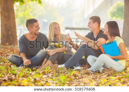 Group of cheerful young students sitting on the ground in a park and studying together