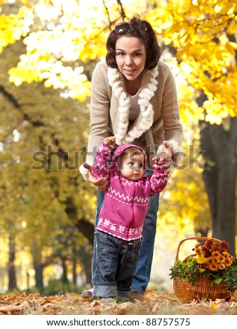 Mother helping her little child to walk on a nice autumn day