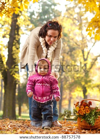 Mother helping her little child to walk on a nice autumn day