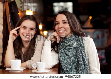 Two beautiful cheerful female friends in a cafe bar