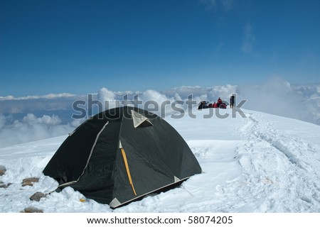 Tent with alpine group on background at 5800m on the way up to camp two (mt. Razdelnaya), Lenin peak, Pamirs, Kyrgyzstan.