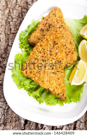 Fried breaded tilapia fish fillet and lemon on white plate