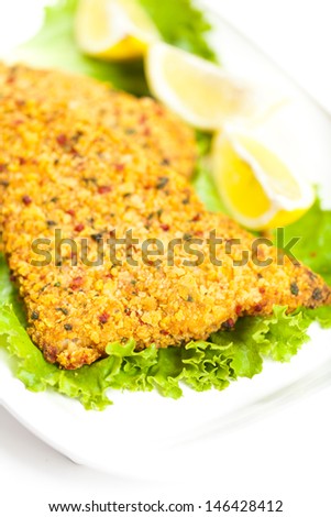 Fried breaded tilapia fish fillet and lemon on white plate