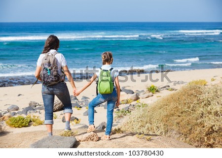 Back view of mother with her daughter walking on a beach, wearing jeans and white shirts