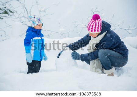 Smiling happy boy with his mother having fun outdoors on snowing winter day in Alps playing in snow.