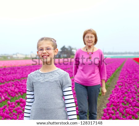 Girl with her grandmother walks between of the purple tulips field