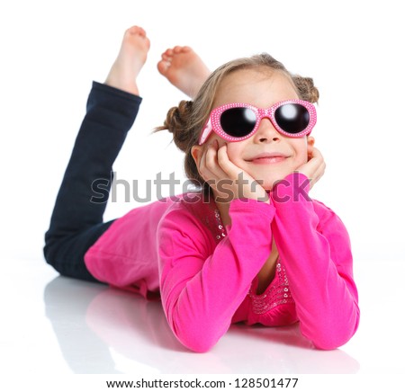 Little fashion girl lying in pink dress and sunglasses. Isolated white backround.