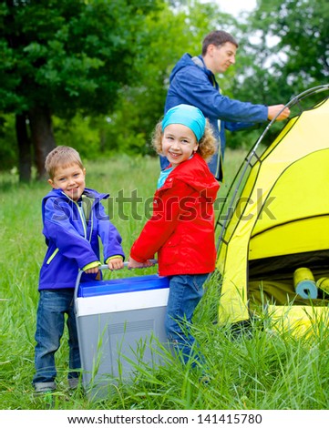 Summer, family camping - lovely sister and brother have a refrigerator with father near camp tent. Vertical view