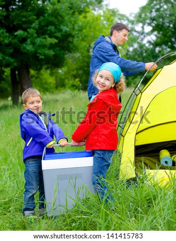 Summer, family camping - lovely sister and brother have a refrigerator with father near camp tent. Vertical view