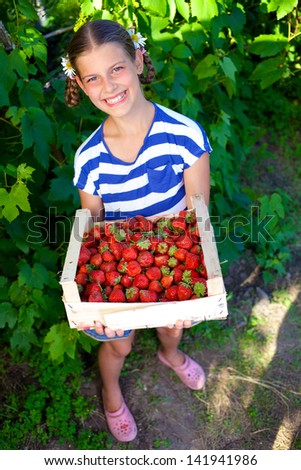 Beautiful smiling girl holding a box of strawberries in garden