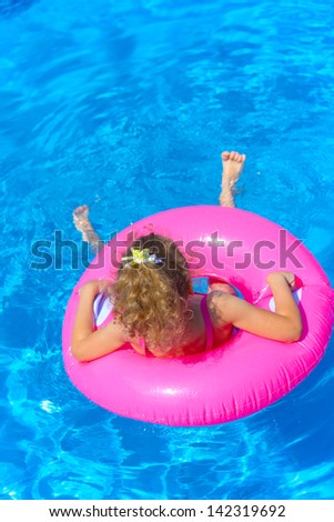 Funny little girl swims in a pool in an pink life preserver