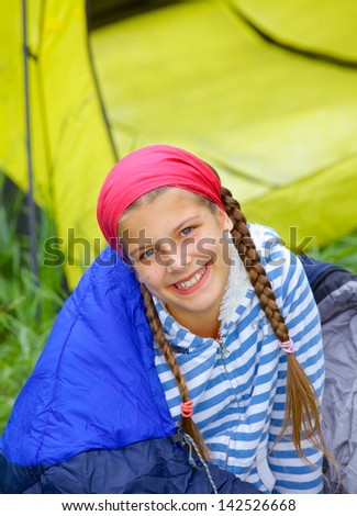 Young girl in a sleeping bag near tent in camping on the nature