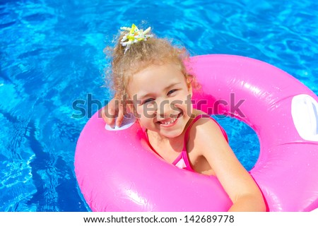 Clouse-up portrait of funny little girl swims in a pool in an pink life preserver