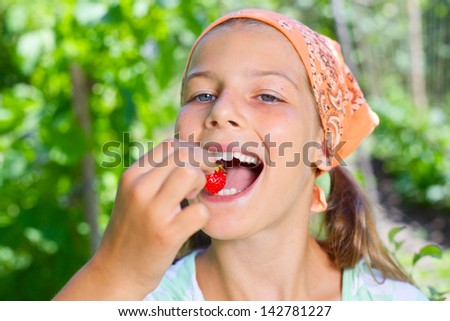 Beautiful little smiling girl eating strawberries in garden