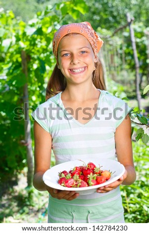 Young girl holding plate with organic natural healthy food produce - strawberries. Vertical view