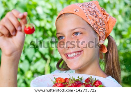 Beautiful little smiling girl eating strawberries in garden