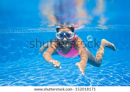 Cute girl swimming in pool underwater and smiling