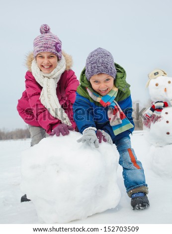 Happy Beautiful Children Building Snowman Outside In Winter Time