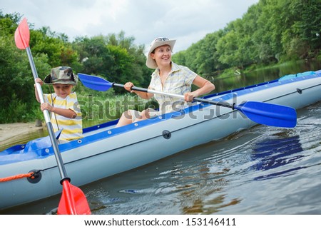 Happy young boy with mother paddling kayak on the river in lovely summer day
