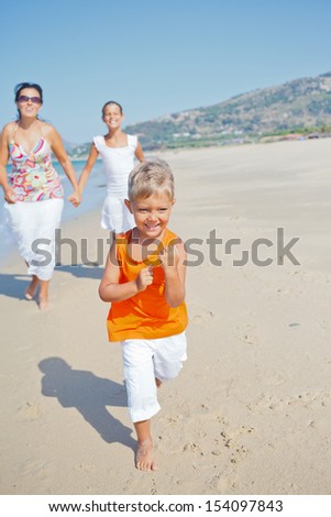 Adorable happy boy with sister and mother running on beach