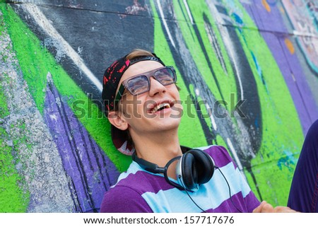 Close-up portrait of happy teens boy with headphones near painted wall listening to music