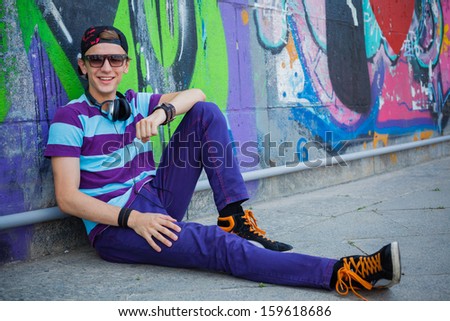Happy teens boy with headphones near painted wall listening to music
