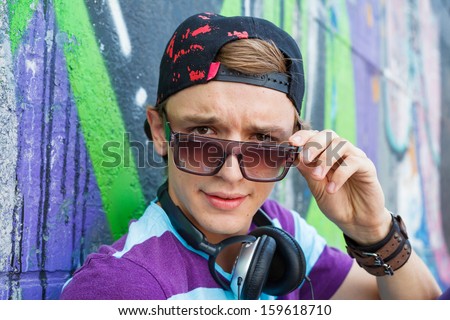 Close-up portrait of happy teens boy with headphones near painted wall listening to music