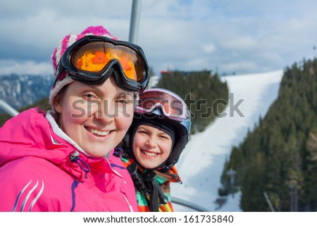 Portrait of happy woman in ski goggles and a helmet with daughter on the ski lift