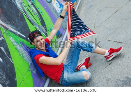 Happy teens boy sitting near painted wall and having fun with american flag