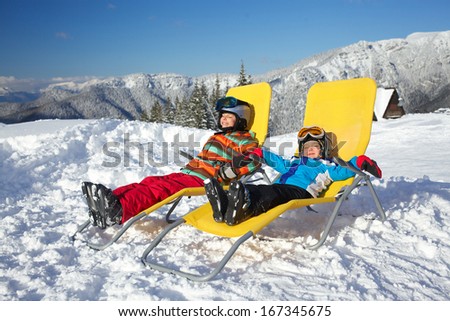 Winter, ski, sun and fun - kids in winter resort resting in the deck chair