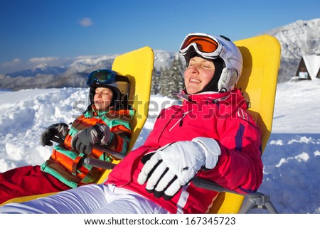 Winter, ski, sun and fun - Portrait of mother with her daughter in winter resort resting in the deck chair