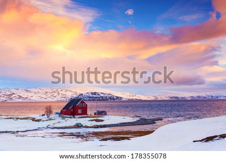 Norway in winter: mountains with red house and the ocean at sunset.
