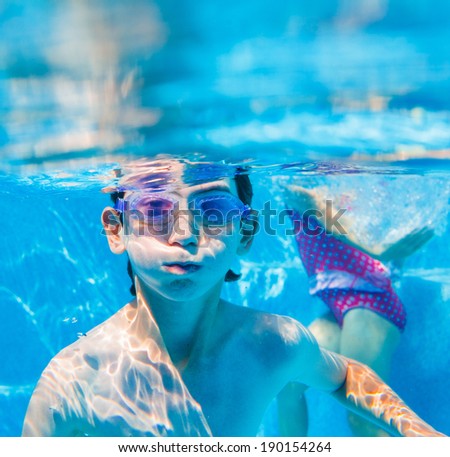 The cute boy swimming underwater in swimming goggles