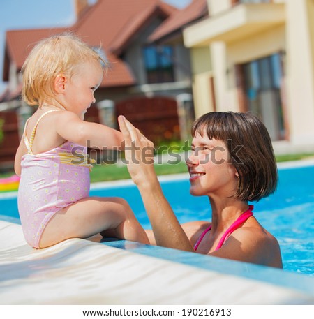 Summer vacations concept. Happy mother and daughter playing in blue water of swimming pool.