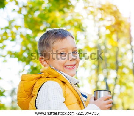 Portrait of Adorable cute boy resting and drinking tea from a thermos in the beauty autumn park