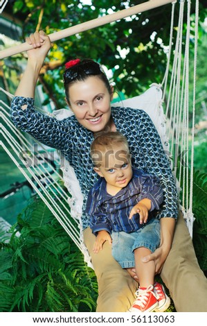 Beautiful young woman swings on a hammock with a young son in their garden