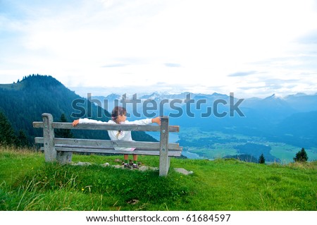 Activities at the top. Sweet girl sitting on a bench and looked at the panorama of mountains. Austria