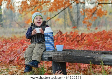 Little cute boy drinks tea from a thermos in the autumn park