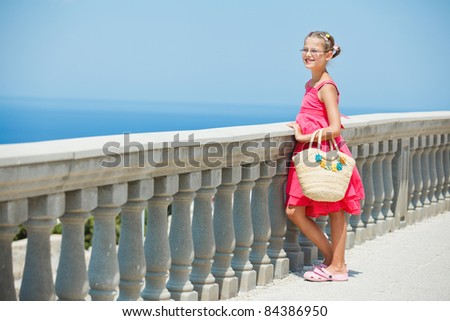 Girl in a pink dress with a straw bag looking at sea