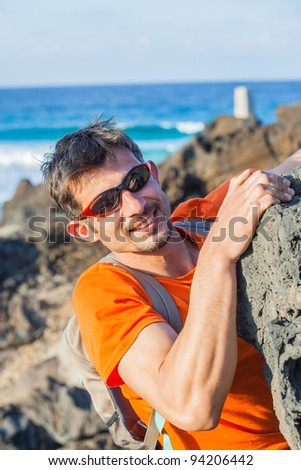 Young man in glasses with backpack climbing indoor wall. Backround sea
