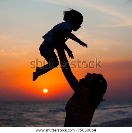 Mother and little son silhouettes on beach at sunset