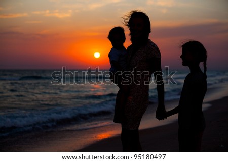 Mother and her kids silhouettes on beach at sunset